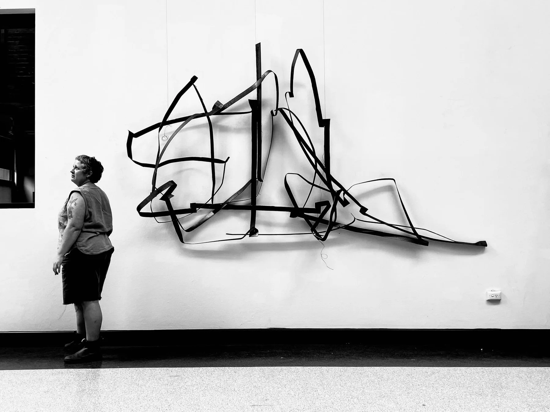 Black-and-white photograph of a figure beside a linear wall installation
